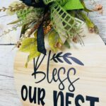 Door hanger that says bless our nest. Greenery attachment with bow on the top.