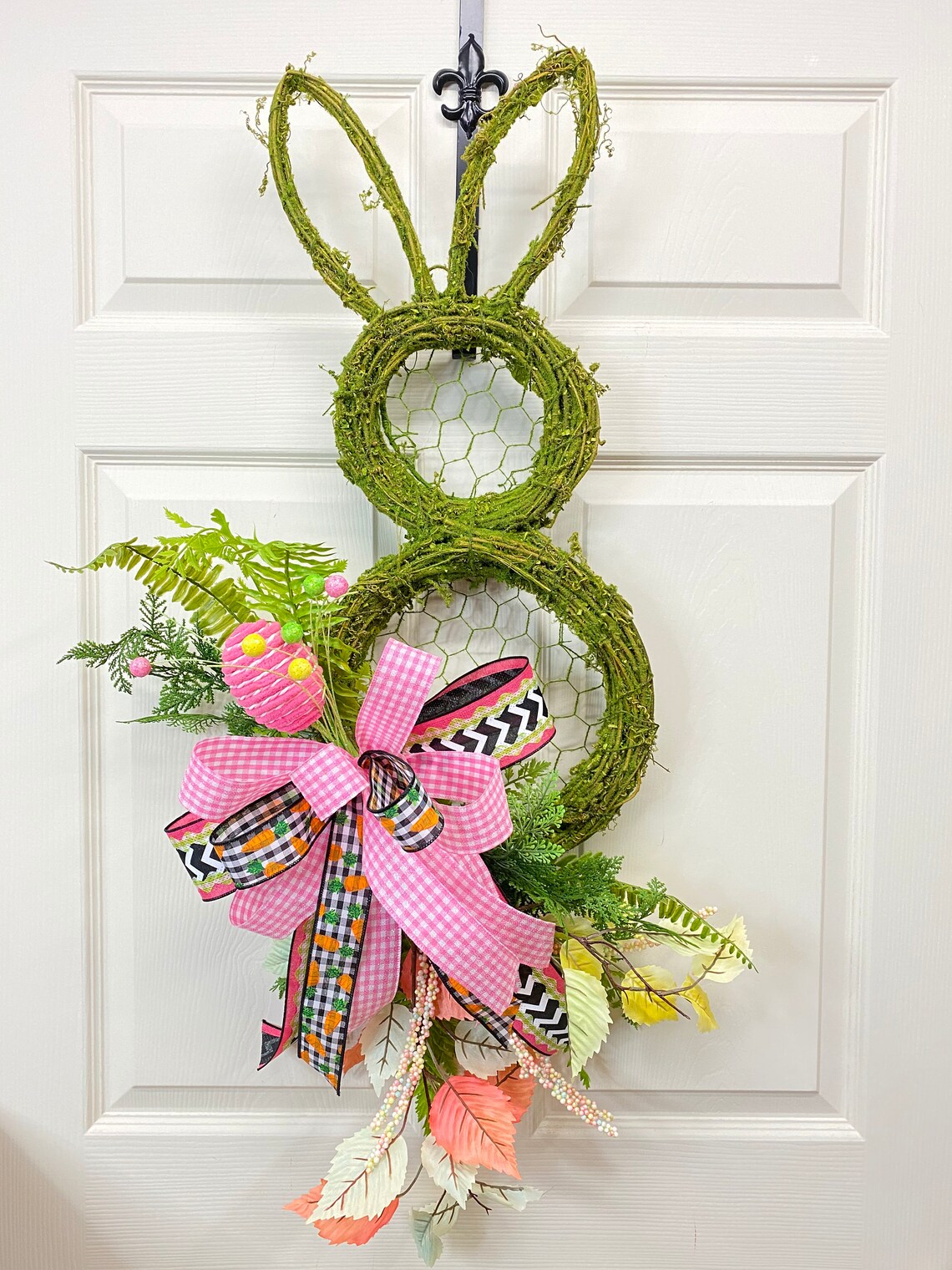 Easter bunny shaped door hanger with greenery and a bow.