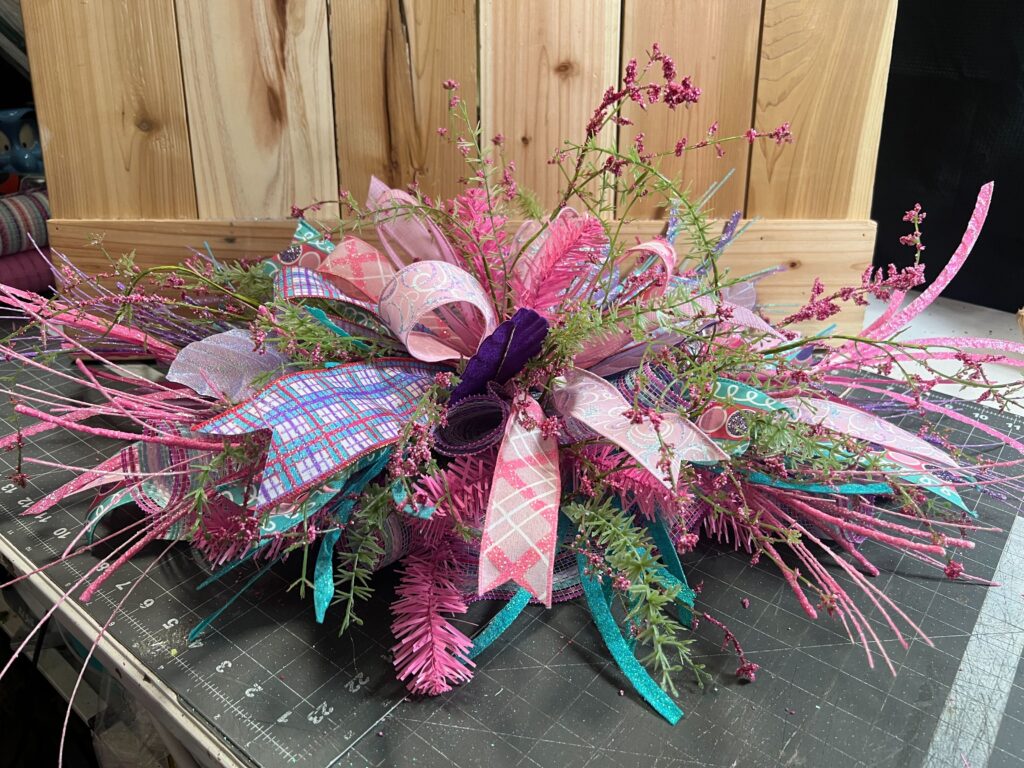 Low floral centerpiece made with the DecoExchange December 2025 wreath supply box, styled with pastel ribbon bows, pink and teal glitter stems, faux greenery, and textured florals arranged for a winter or Easter table display.
