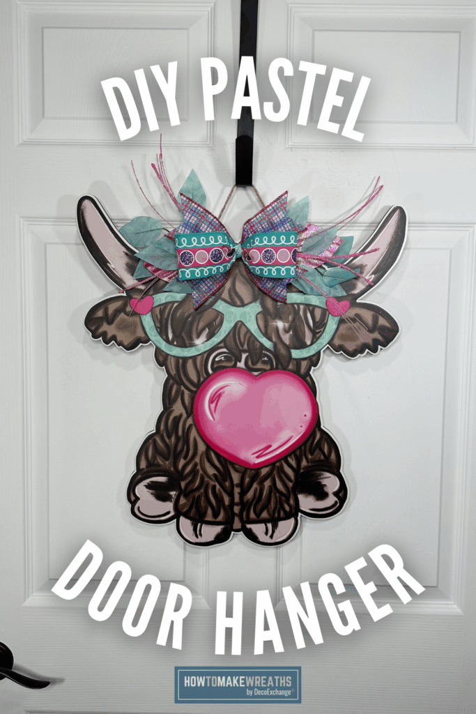 Pastel cow door hanger with teal glasses and pink heart, decorated with layered ribbon bow in turquoise, pink, and purple on a white front door.
