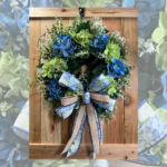 finished hydrangea wreath with blue and green flowers and layered greenery displayed on a wooden door