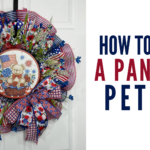 Tutorial thumbnail showing a full patriotic pancake petite wreath with layered red, white, and blue deco mesh, mixed flag and floral ribbon, blue and red flower stems, and a round teddy bear American flag focal sign, hung on a white door beside bold text reading How to Make a Patriotic Pancake Petite.