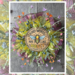 Small pancake wreath made with yellow mesh, pink and black striped mesh, wildflower florals, and a round wood bee sign that says Kind Words Are Like Honey hanging on a rustic wood background.