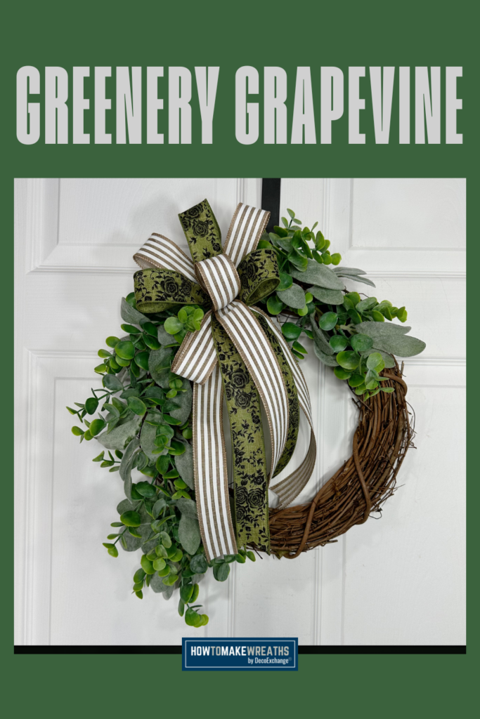 A grapevine wreath base fully covered in green eucalyptus and lambs ear foliage with a green floral and striped ribbon bow at the top, displayed on a white door under a green background with the text Greenery Grapevine.