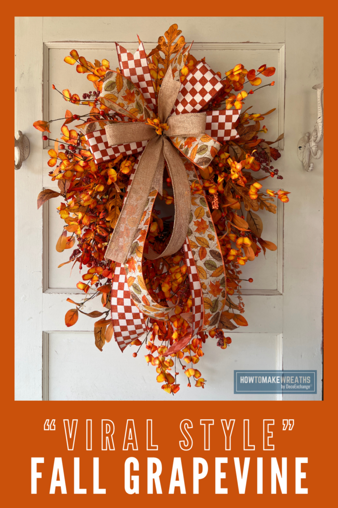 Rust and white checkered ribbon, warm burlap, and a leaf print ribbon come together in one layered bow on this fall grapevine swag. Orange and yellow florals, oak leaves, and berry picks fill out the teardrop shape for a full, textured look that stands out on any front door. See the full tutorial at HowToMakeWreaths.com. #FallGrapevine #AutumnWreath #ViralStyle #FallDecorIdeas #WreathMaking #DecoExchange #CheckeredRibbon #FrontDoorSwag #FarmhouseDecor #HowToMakeAWreath
