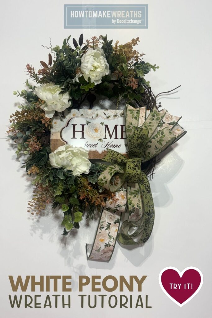 A grapevine wreath covered in layered deep green and rust-toned mixed greenery, eucalyptus, and fern stems, accented with three large white peony blooms, centered with a Home Sweet Home sign featuring a white peony and burlap border, finished with a layered bow in green botanical and cream peony print ribbon with long cascading tails, displayed against a white wall.