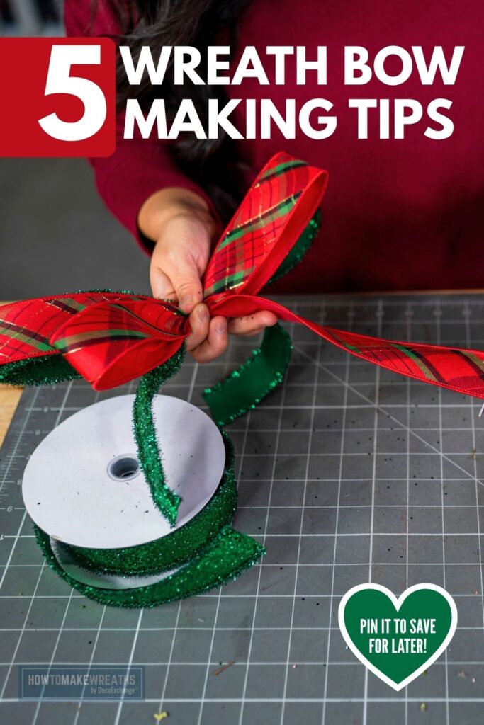 Hands tying a red and green plaid wired ribbon bow on a gray cutting mat, with a spool of green tinsel ribbon in front. Text overlay reads 5 Wreath Bow Making Tips, with a Pin It to Save for Later heart and the How to Make Wreaths by DecoExchange logo.